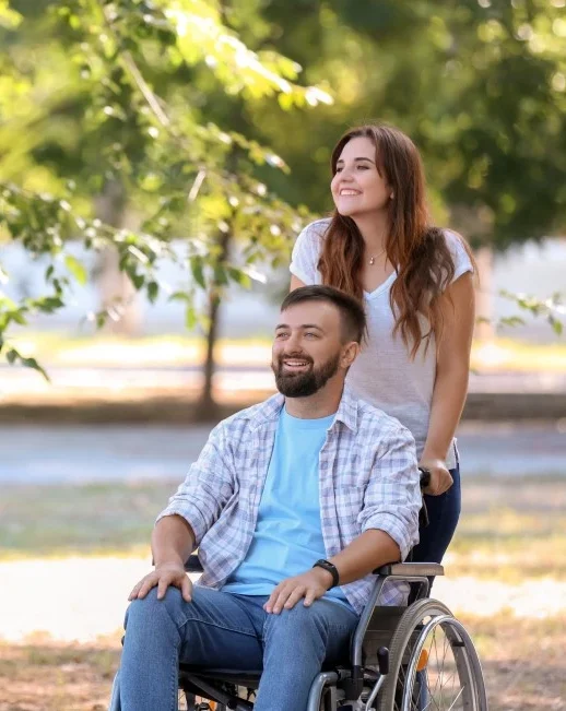 Disabled man sitting in his wheelchair and his support worker smiling while outdoors