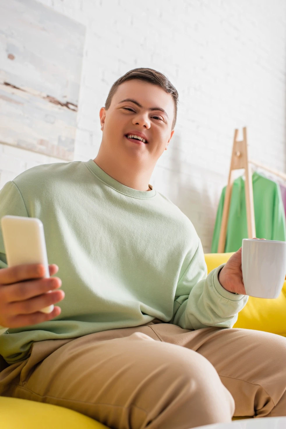 A disabled man smiling while holding a coffee mug and mobile phone
