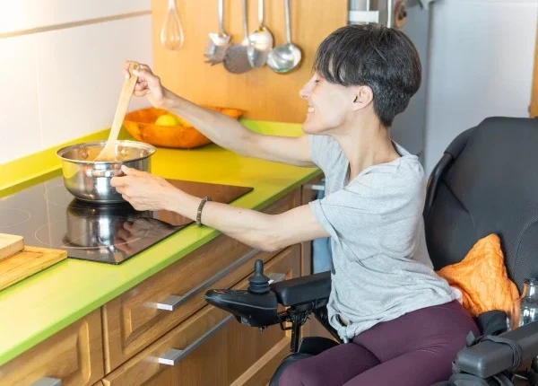 A disabled woman sitting in her wheelchair cooking in the kitchen