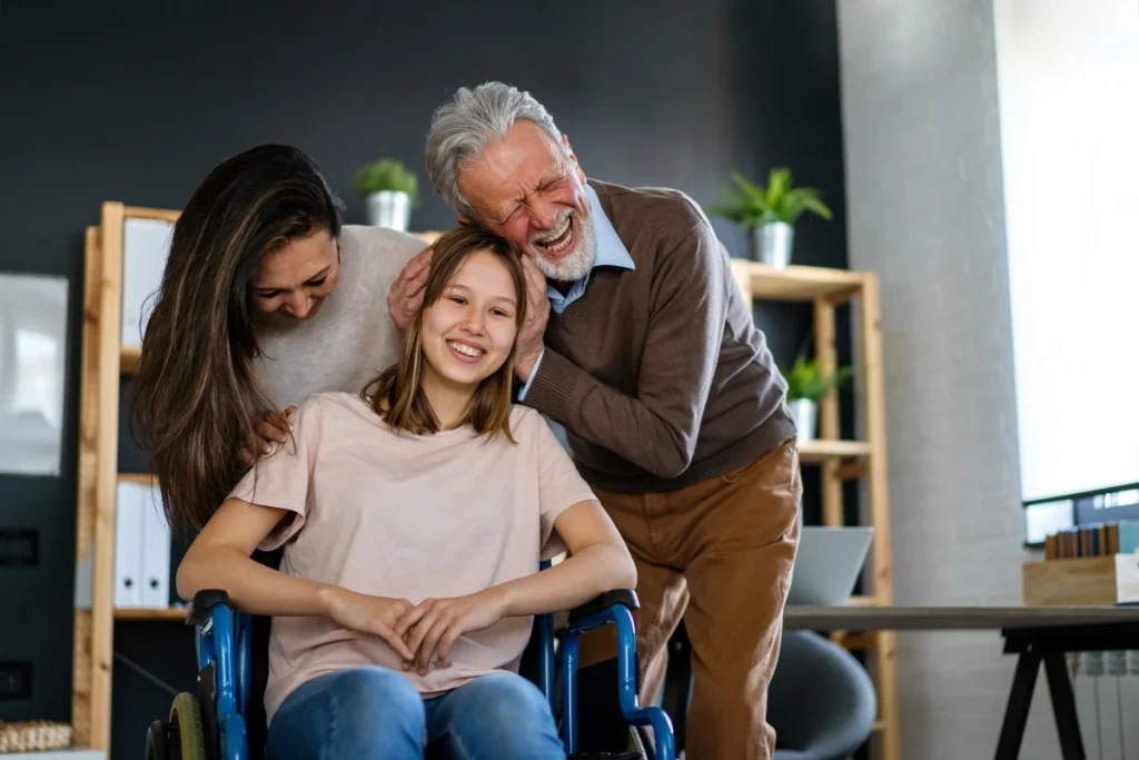 A disabled woman sitting in her wheelchair and her parents hugging her