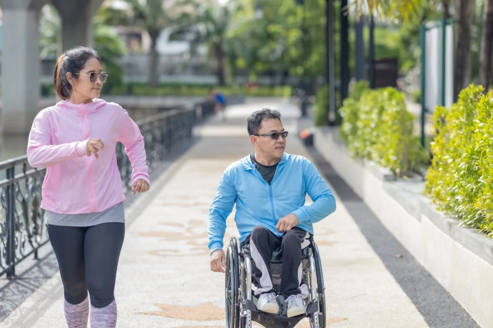 A disabled man sitting in his wheelchair and his support worker going for a walk